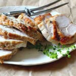 A cooked boneless turkey breast roast sliced on a white platter.