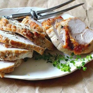 A cooked boneless turkey breast roast sliced on a white platter.