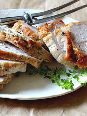 A cooked boneless turkey breast roast sliced on a white platter.