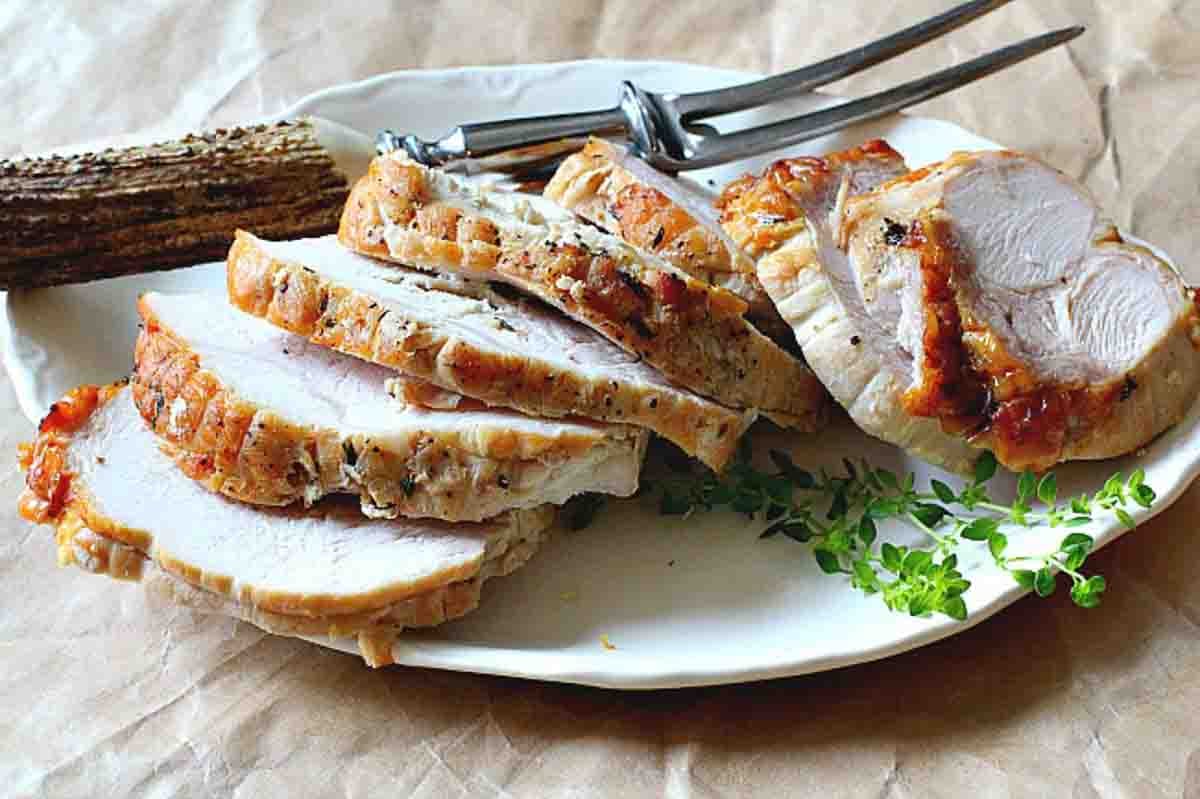 A cooked boneless turkey breast roast sliced on a whte platter.