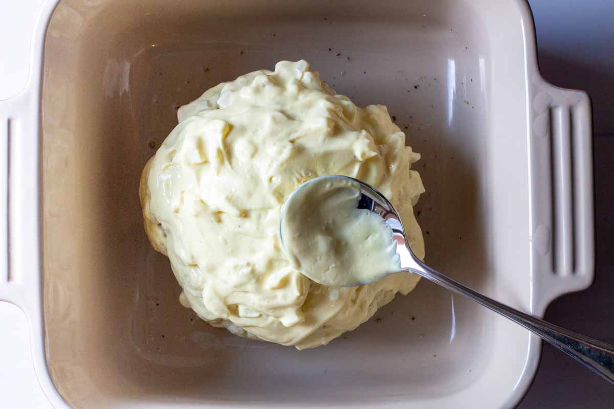 spreading mayo sauce over a whole head of cauliflower that's been cooked in the microwave