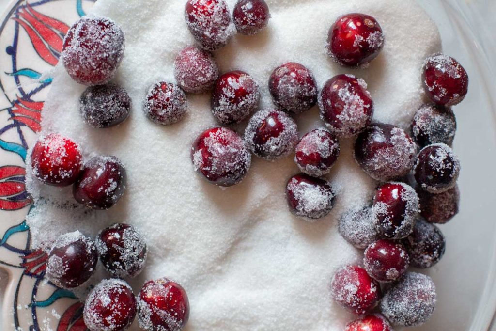 Rolling sticky cranberries in sugar to make sugared cranberries