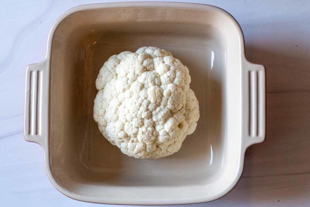 Whole head of cauliflower in a deep casserole dish ready to cook in the microwave