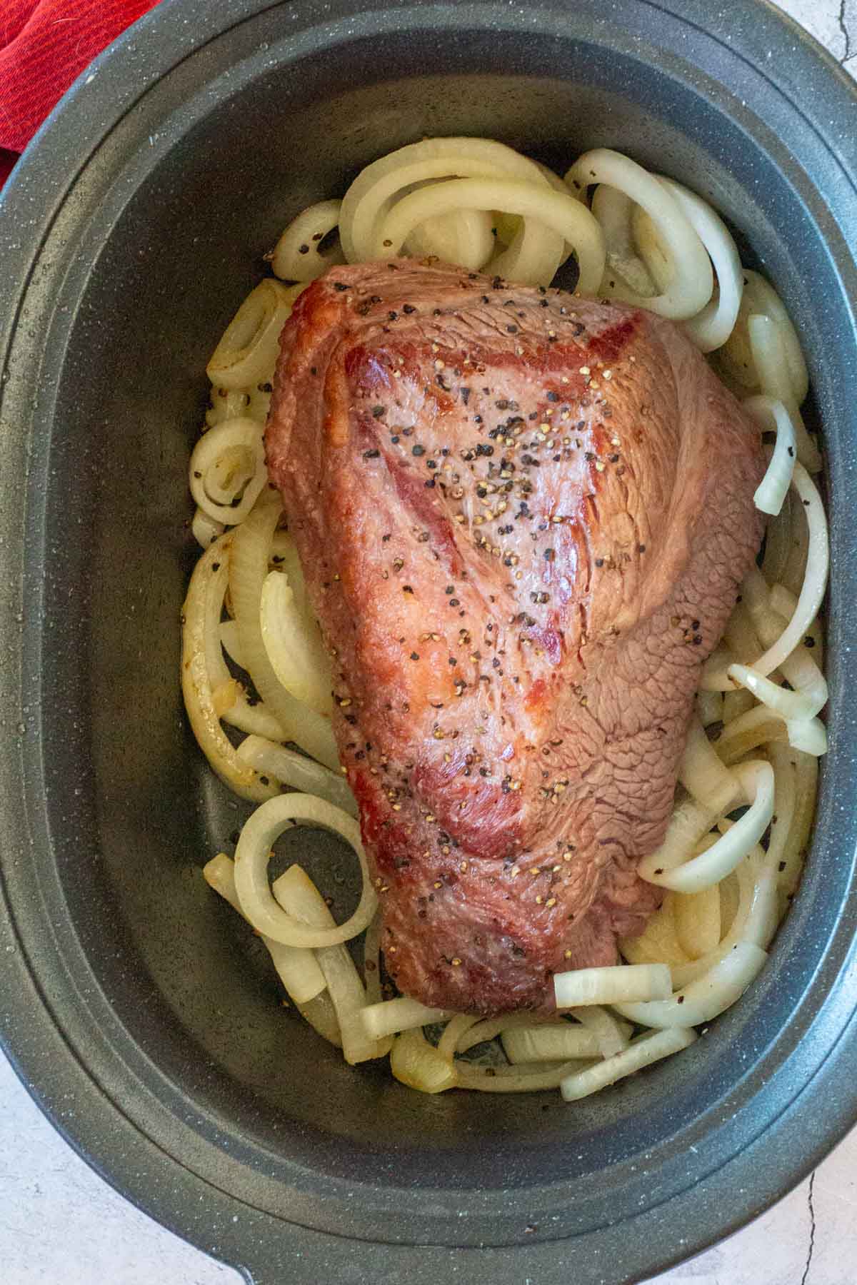 A beef brisket in a crock pot sitting on a bed of fried onions.