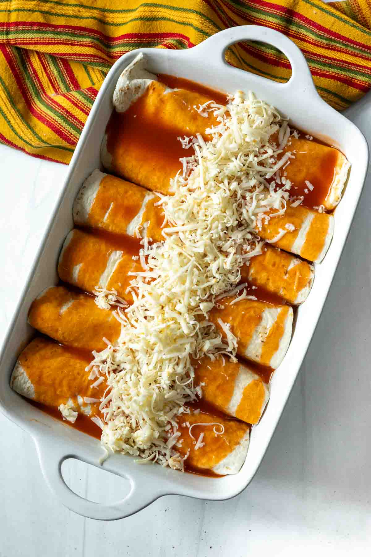 Adding cheese topping to enchilada style burritos before baking.