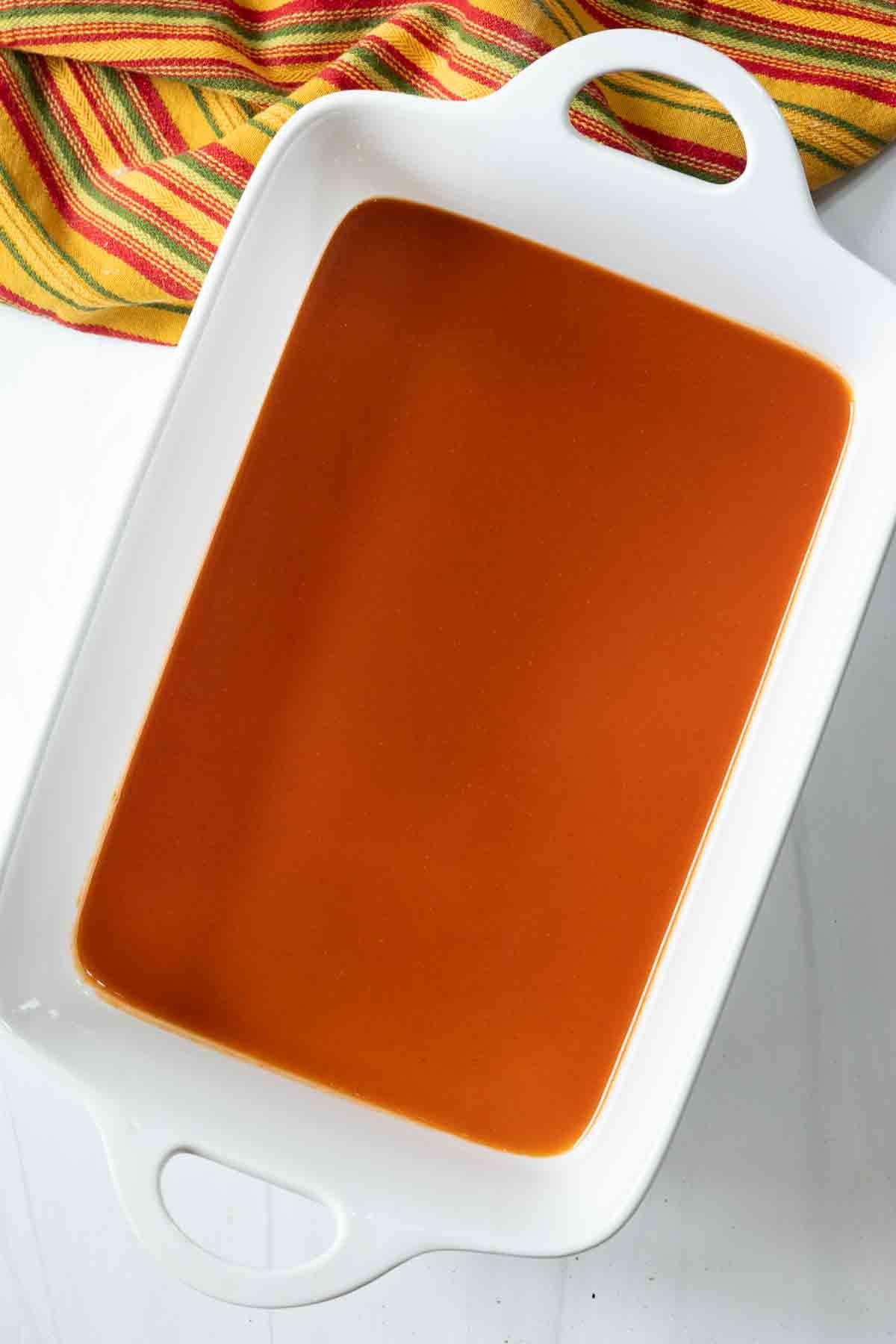 Pouring enchilada sauce in the bottom of a casserole dish to bake enchilada burritos.
