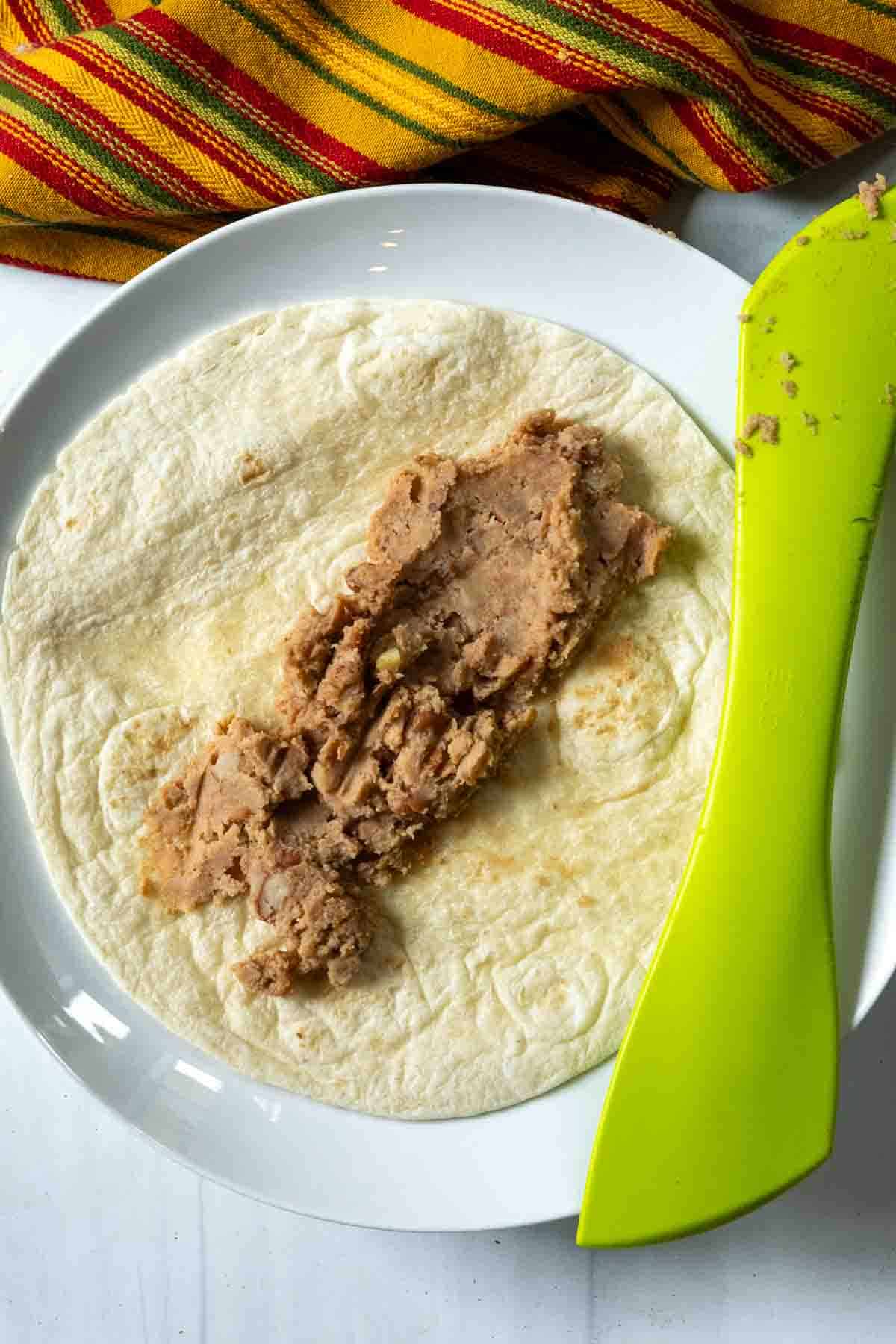 Spreading refried beans on a flour tortilla to make burrito enchiladas.