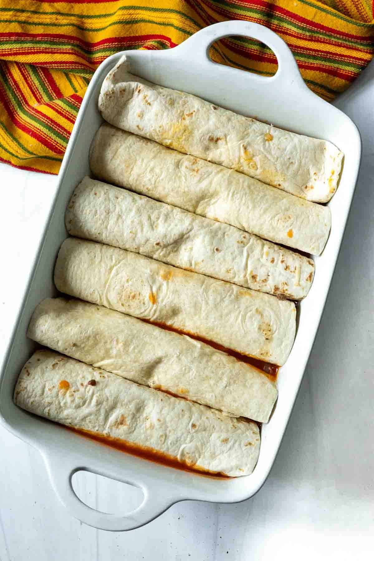 Placing rolled burritos into a casserole dish to make enchilada style burritos.