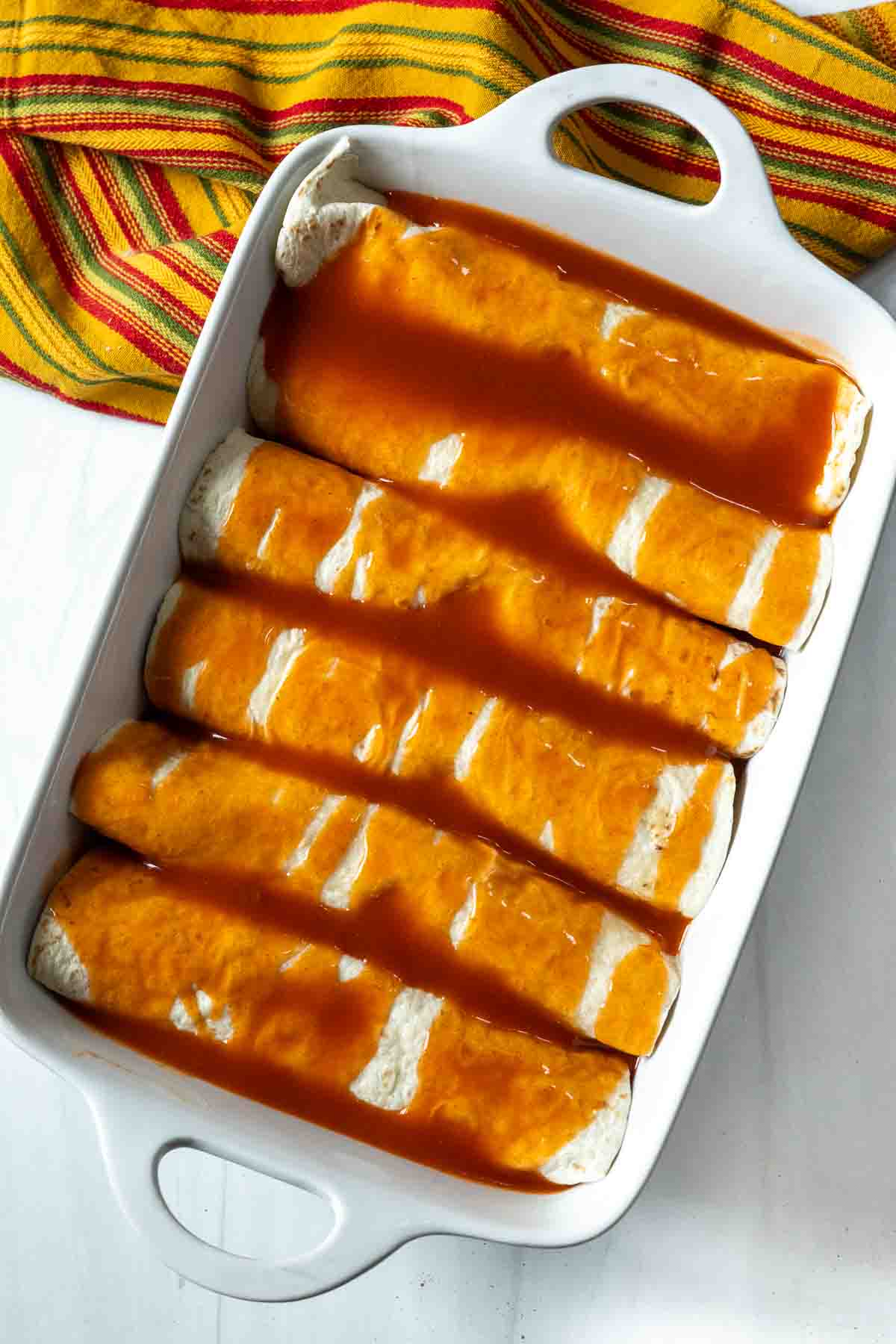 Burritos in a casserole dish covered with enchilada sauce.
