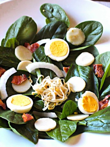 Spinach salad garnished with sliced hardboiled eggs and bacon
