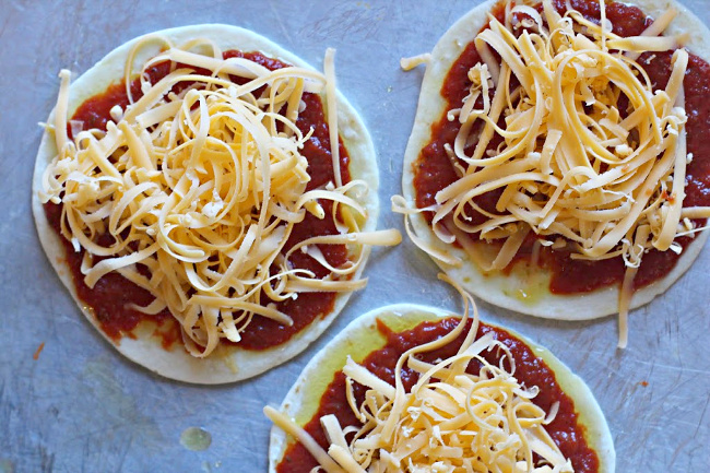 Building flour tortilla pizza appetizers. Adding the cheese