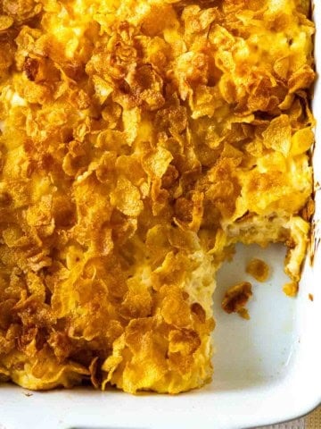 Cheesy potatoes with Corn Flakes in a white casserole dish.