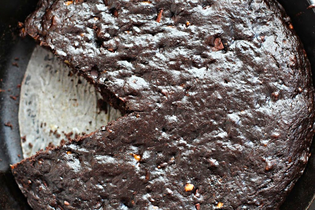 Chocolate banana bread recipe cooked in a cast iron skillet. Lined with parchment paper and a wedge cut out.