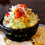Spicy Guacamole recipe with bacon lettuce and tomato served in a brown pottery bowl with tortilla chips