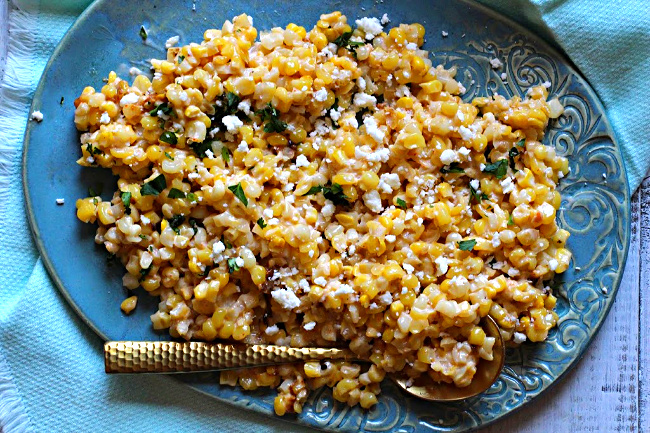 Mexican corn salad sprinkled with Mexican Crumbling Cheese and cilantro. Served on a blue hand made ceramic platter with a gold spoon.