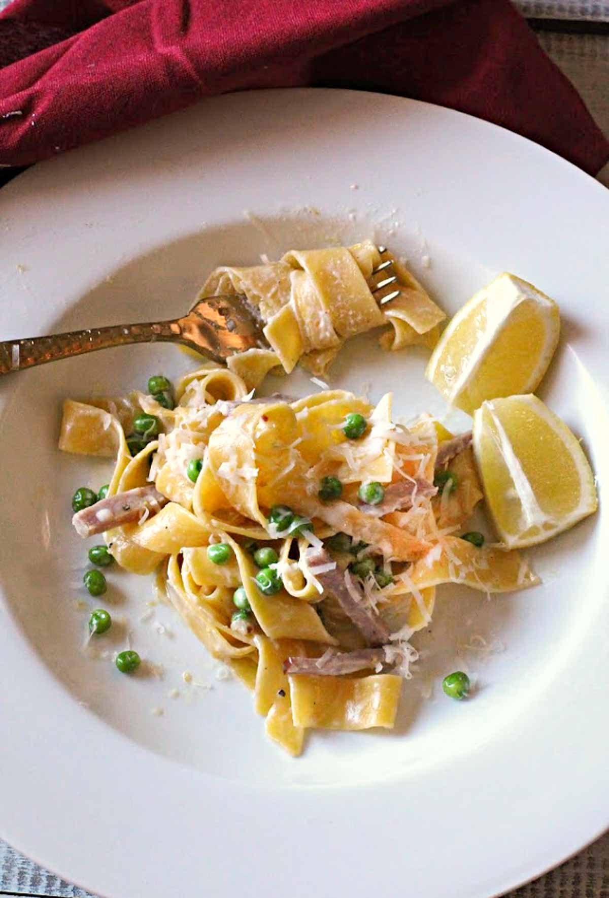 Pappardelle noodles in a lemon cream sauce with peas and ham served in a white pasta bowl with a gold fork