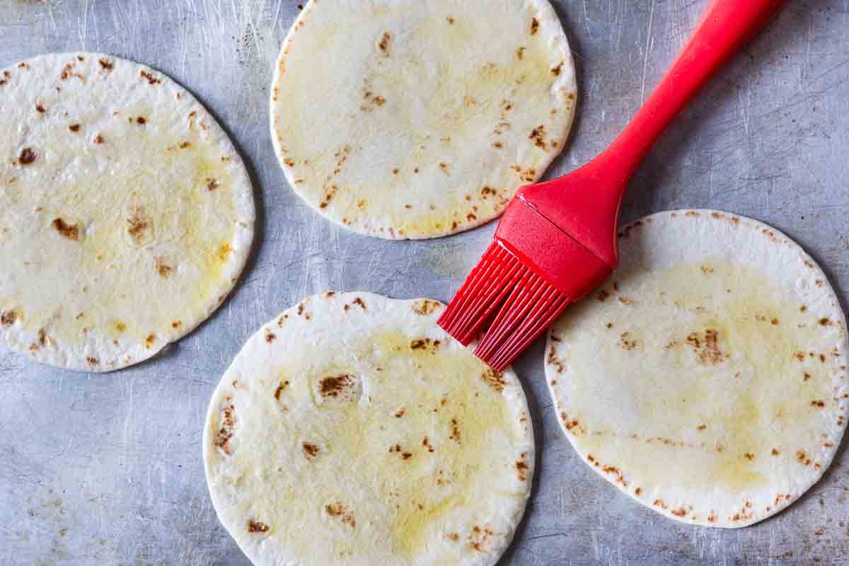 Step 1: oiling flour tortillas to make tortilla pizzas.