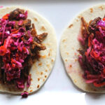 braised beef tacos on a white flour street taco shell topped with cabbage carrot slaw