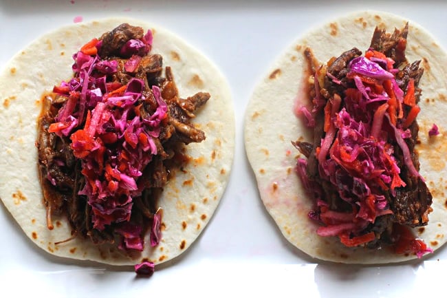 braised beef tacos on a white flour street taco shell topped with cabbage carrot slaw