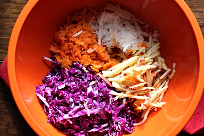 shredded Red cabbage, shredded carrot, shredded gala apple, shredded onion in an orange bowl.