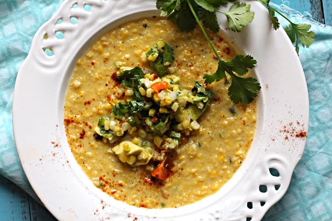 Fresh sweet corn soup topped with roasted corn guacamole served in a white lattice bowl garnished with a sprig of cilantro