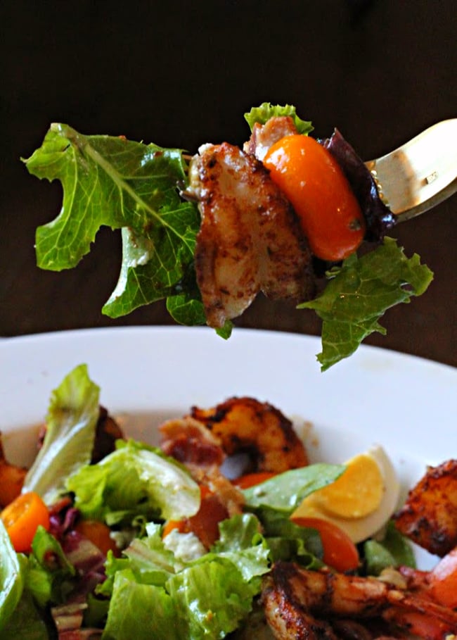 Spring greens, blackened shrimp and orange petite cherry tomato on a gold fork.