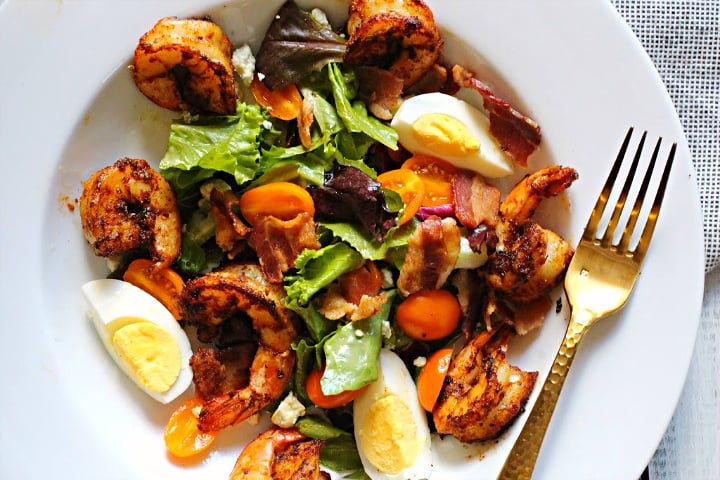 Blacked shrimp salad in a large wide rimmed salad bowl with hard boiled eggs, spring greens, and applewood smoked bacon. With champagne vinaigrette.