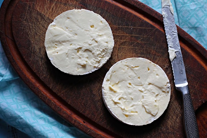 Two halves of a wheel of brie cheese on a wooden cutting board.