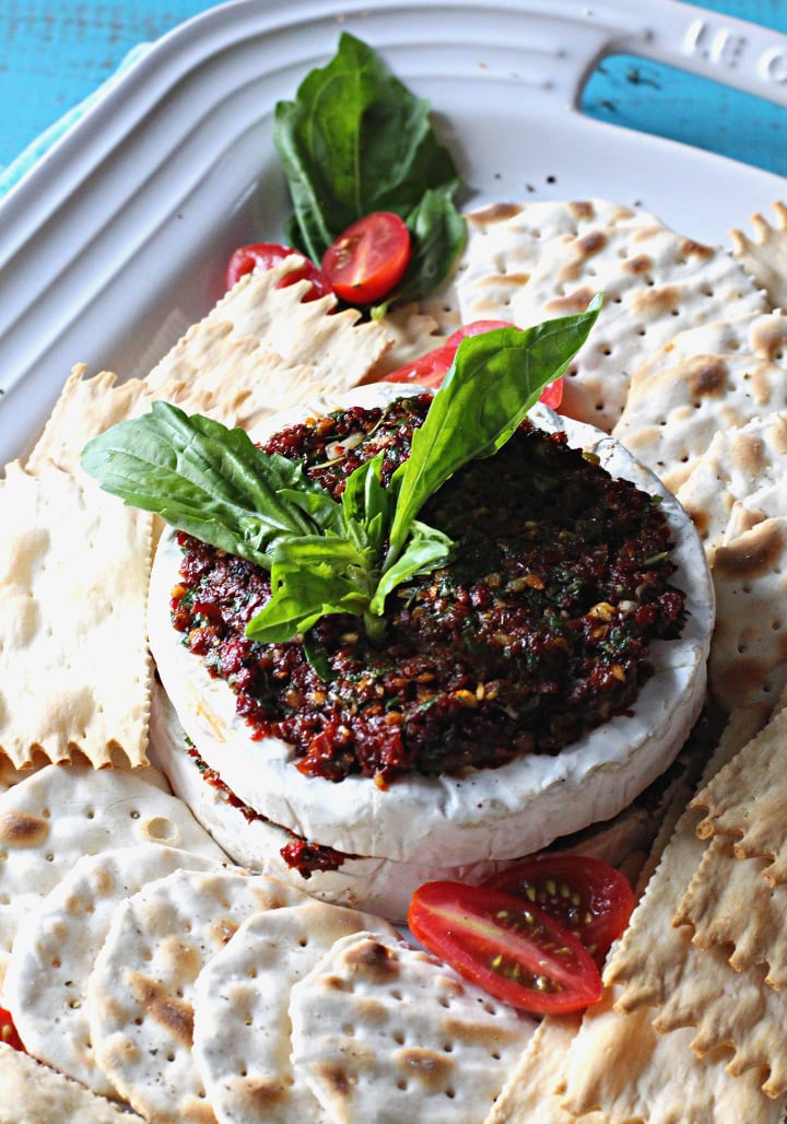 Sun dried Tomato appetizer with basil and garlic stuffed in a wheel of brie cheese surrounded by water crackers.