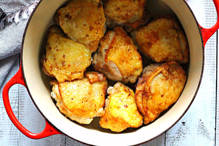 Browned chicken thighs in a Red Le Creuset Dutch Oven for Chicken Marengo.