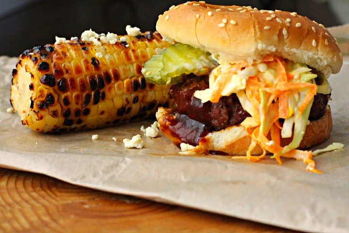 Texas burger recipe, a Bobby Flay recipe topped with homemade coleslaw, pickles and bbq sauce. Sided with grilled corn.