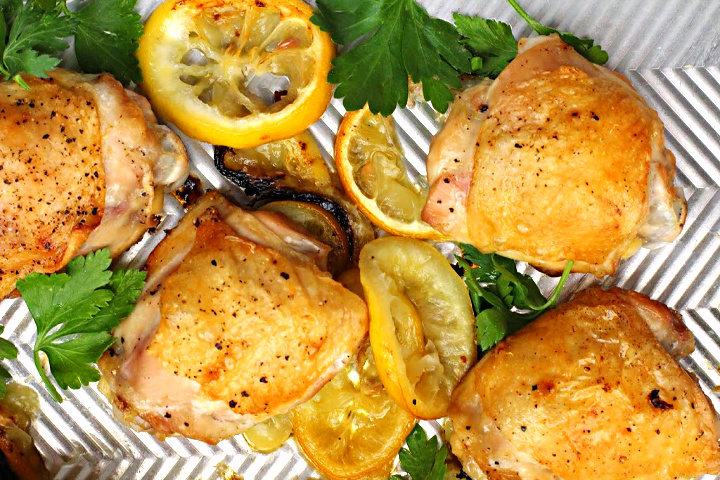 Crispy baked lemon chicken thighs on a sheet pan with lemon slices and pieces of fresh parsley