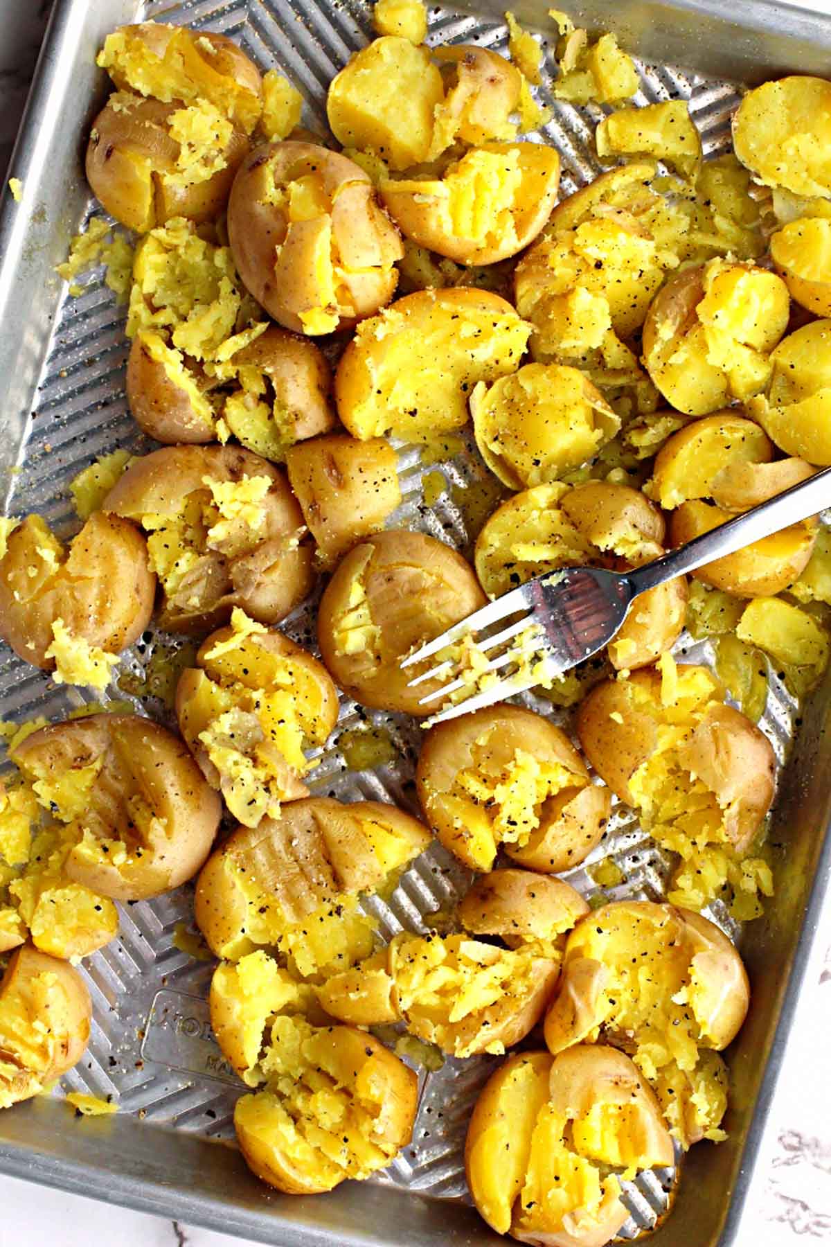 yukon gold potatoes on a sheet pan getting smashed by a fork
