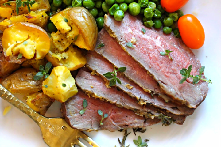 Sliced Tri-tip steak roasted in the oven served with smashed potatoes and peas.
