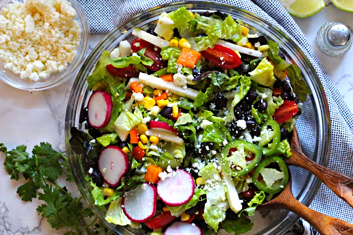 Southwestern salad served in a glass serving bowl with radishes, black beans, corn, jicama, jalapeno rings, cotija cheese.