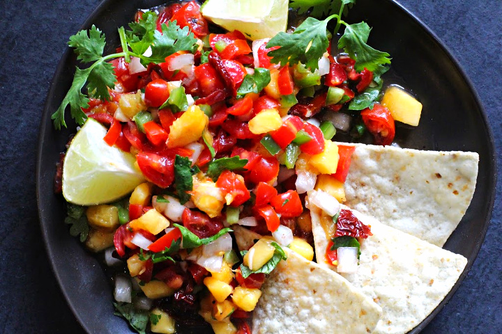 Spicy peach salsa on a dark gray plate served with tortilla chips and limes.