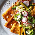 Street style folded enchiladas in red chile sauce topped with radish and crunchy vegetables