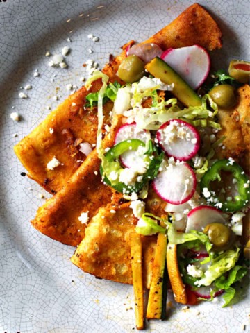 Street style folded enchiladas in red chile sauce topped with radish and crunchy vegetables
