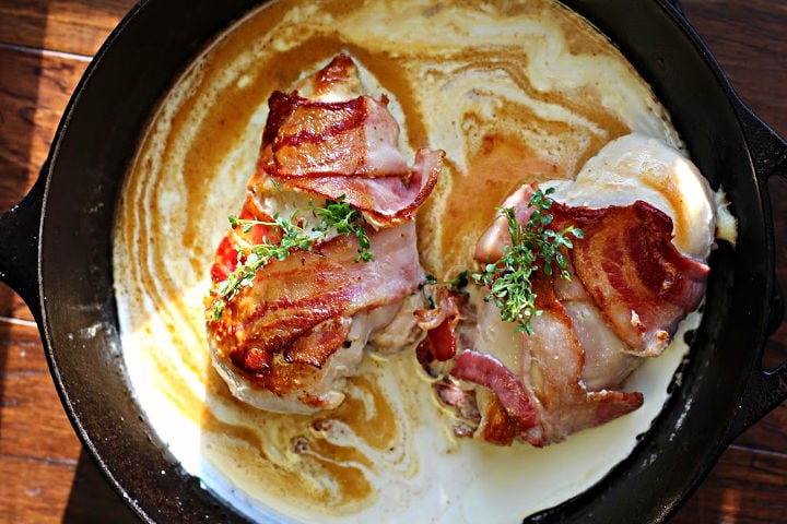 Bacon wrapped chicken breast in a garlic cream sauce in a cast iron skillet.