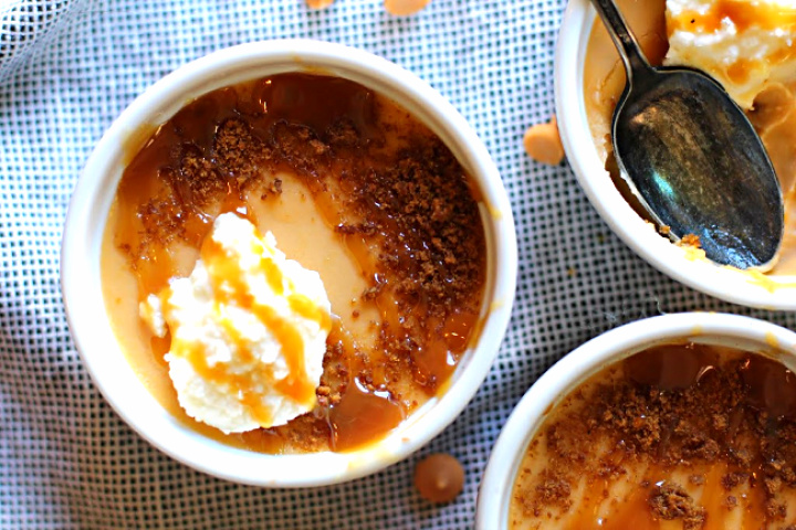 Homemade butterscotch pudding served in small white ramekin bowls topped with whipped cream and caramel sauce.