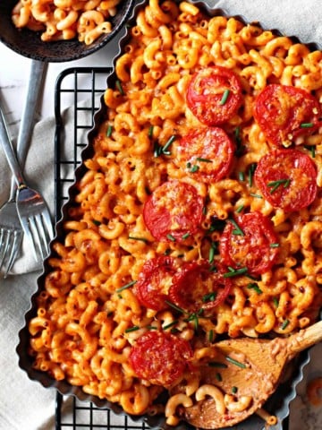 A casserole dish filled with Mexican Macaroni and Cheese topped with sliced tomatoes