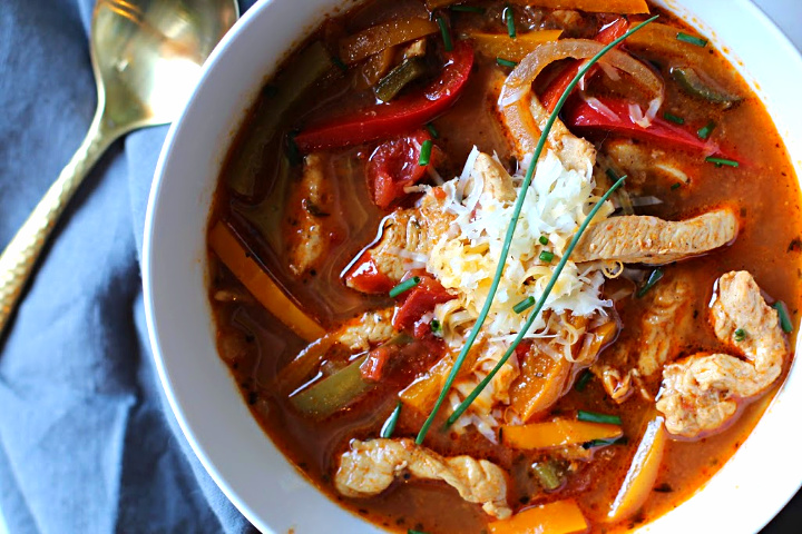 Chicken fajita soup topped with grated Mexican cheese, served in a white soup bowl with a bowl full of tortilla strips for garnish.