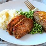 Individual meatloaf recipe for spicy meatloaf. Served on a white plate with mashed potatoes and peas.