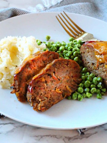 Individual meatloaf recipe for spicy meatloaf. Served on a white plate with mashed potatoes and peas.