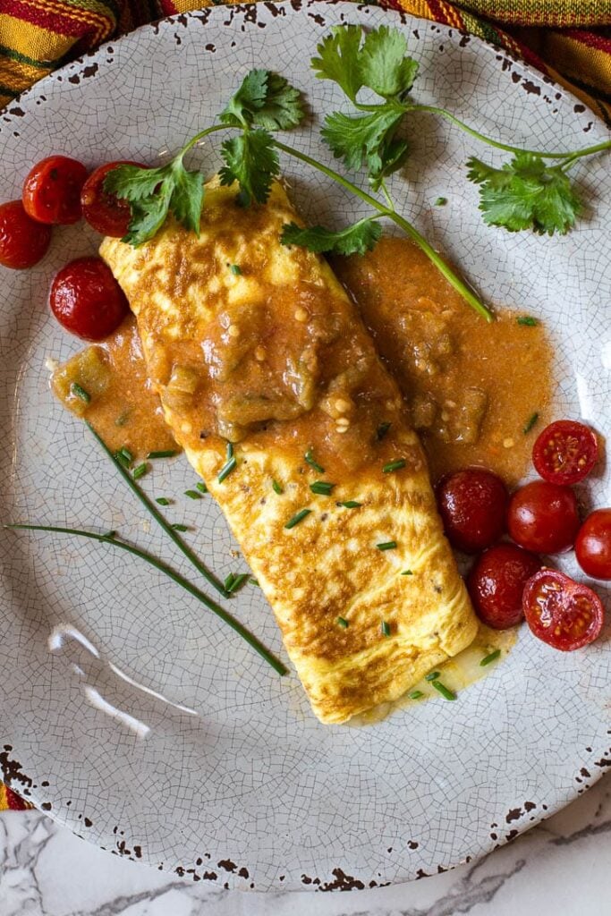 Cheese Omelette smothered in hatch green chile sauce and garnished with cherry tomatoes and cilantro