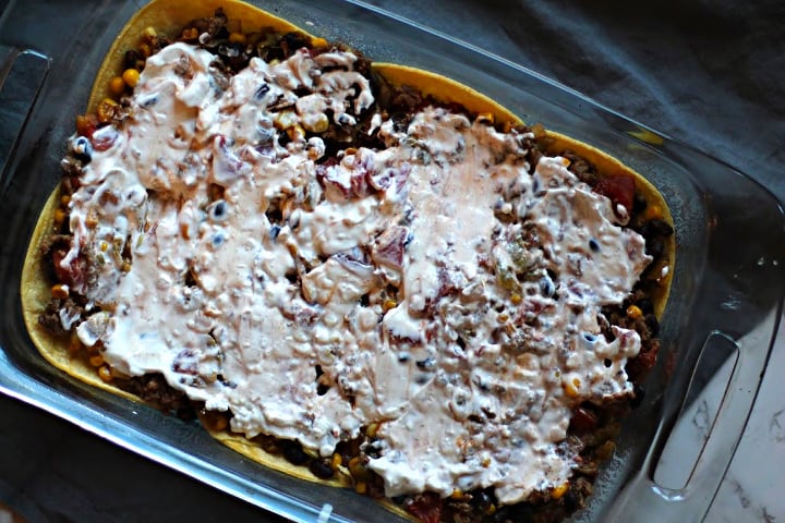 Layered Mexican Casserole with Ground Beef and Corn tortillas topped with sour cream.