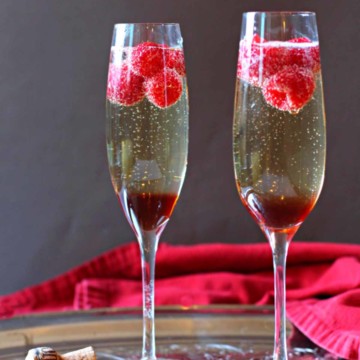 Raspberry Chambord Prosecco cocktail served in two champagne glasses with raspberries.
