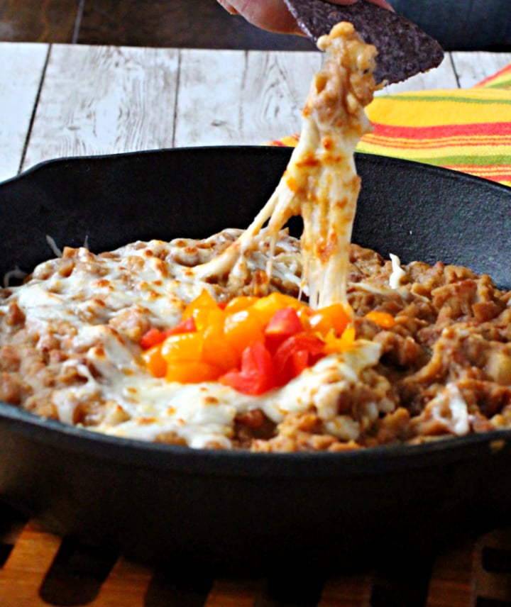 Refried beans in a cast iron skillet topped with cheese and used as a dip appetizer
