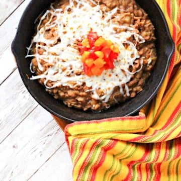 Instant pot refried beans served in a cast iron skillet topped with cheese and chopped tomatoes