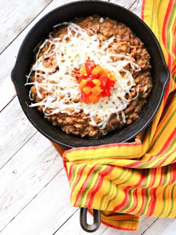 Instant pot refried beans served in a cast iron skillet topped with cheese and chopped tomatoes